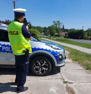 Policjant mierzący prędkość stojący przy radiowozie .