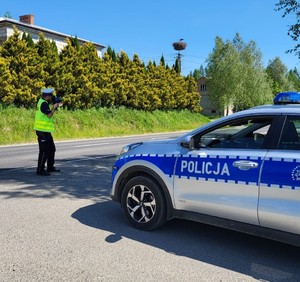 Policjant mierzący prędkość stojący przy radiowozie.