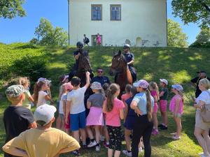 Uczestnicy pikniku przy radiowozie z policjantami na koniach.