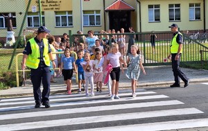 Policjanci wraz z dziećmi na przejściu dla pieszych.