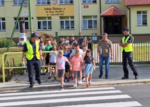 Policjanci wraz z dziećmi na przejściu dla pieszych.