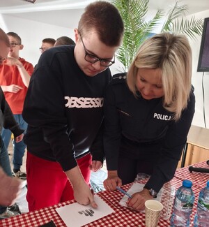 Chłopiec wraz z funkcjonariuszką KPP w Strzyżowie odbijający na białej kartce papieru odciski palców
