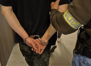 Zatrzymany 19-latek z założonymi kajdankami na ręce trzymane z tyłu.