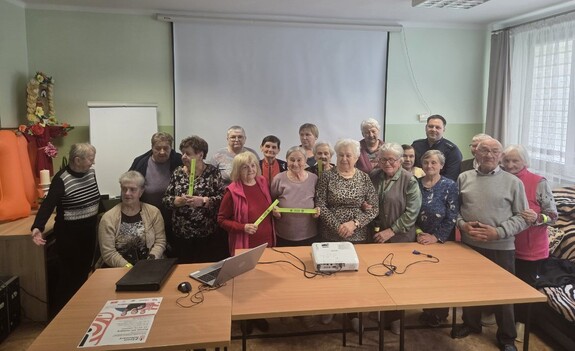 Dzielnicowy wspólnie z seniorami uczestniczącymi w spotkaniu.