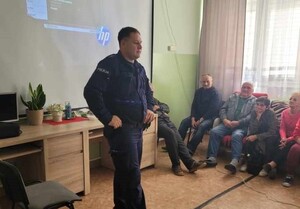 Dzielnicowy prowadzący spotkanie w tle jest wyświetlana prezentacja.