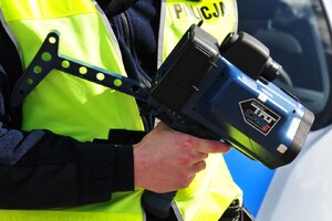 Policjant trzymający w ręce miernik prędkości pojazdu.