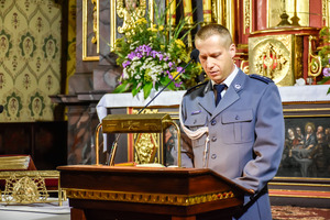 Policjant w mundurze wyjściowym stojący przy ambonie w kościele.